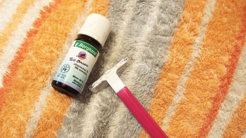 Ein Fläschchen Teebaumöl liegt neben einem pinken Kamm auf einem gestreiften Handtuch, bereit zur Anwendung gegen Haarwurzelentzündungen.