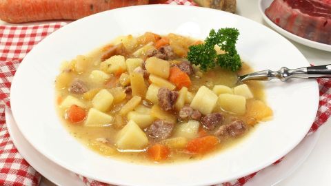 Ein köstlicher Steckrübeneintopf mit Gemüse und Fleisch wird auf einem weißen Teller serviert, umgeben von frischen Zutaten.