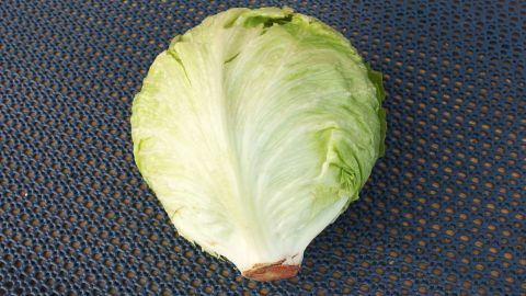 Ein frischer Eisbergsalat liegt auf einer dunklen Unterlage und wartet darauf, vorbereitet zu werden.