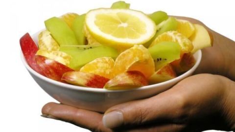Hände halten einen Obstteller mit Apfelscheiben, Kiwi, Mandarine und Zitronenscheiben, bereit zum Fernsehen.