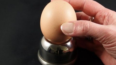 Ein gekochtes Ei wird mit einer Hand vor einer Metallunterlage gehalten, um es stressfrei abzupellen.