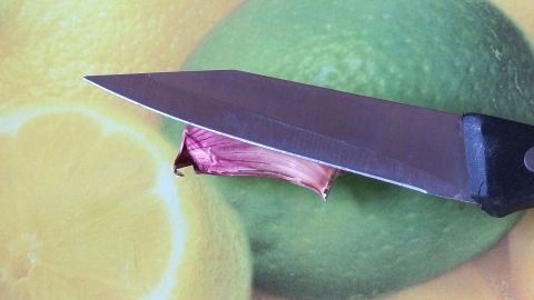 Eine Knoblauchzehe wird mit einem Messer auf einer bunten Unterlage aus Zitrusfrüchten geschnitten, um das Schälen zu erleichtern.