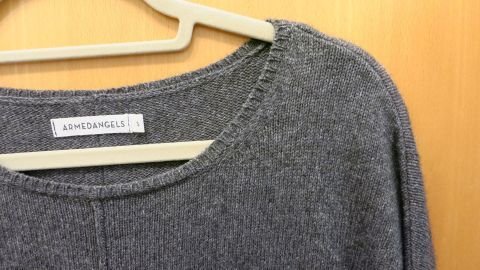Falls dein Strickpulli nach dem heißen Waschen eingegangen ist, kannst du ihn über Nacht in lauwarmem Wasser mit etwas Haarwaschmittel einweichen lassen. Am nächsten Morgen wieder vorsichtig in Form bringen. Ein grauer Wollpulli hängt an einem Kleiderbügel, zeigt eine nicht perfekte Passform aufgrund des Einlaufens.