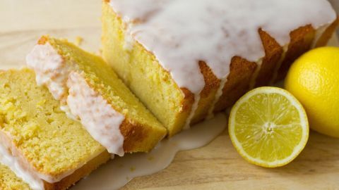 Ein saftiger Zitronenkuchen liegt auf einem Holzbrett, mit einer Glasur und einer halbierten Zitrone daneben.