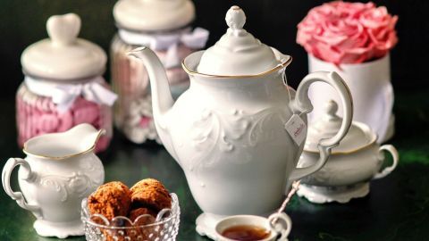 Eine elegante Teekanne mit Tassen steht auf einem grünen Tisch, umgeben von Süßigkeiten und Blumen.