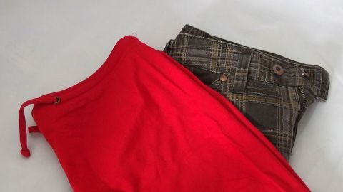 Ein rotes Kleidungsstück liegt neben einer karierten Hose auf einem weißen Untergrund, ideal für Klamotten tauschen statt kaufen.