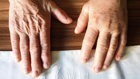 Zwei Hände liegen flach auf einer Holzoberfläche, der Kontrast zeigt verschiedene Hauttöne und Altersmerkmale.