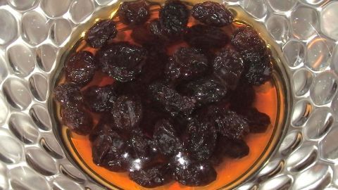 Schwarze Rosinen schwimmen in einer goldfarbenen Rum-Soße, dekorativ in einer glänzenden Schüssel angerichtet.