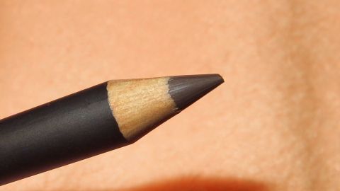 Ein verzogener Kajalstrich lässt sich mit einem Wattepad und etwas Creme gut entfernen. Ein Kajalstift liegt auf einem weichen, orangefarbenen Hintergrund, bereit zum Kajal entfernen.