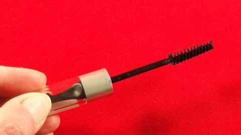 Eingetrocknete geschlossene Wimperntusche zehn Minuten in heißes Wasser legen. Danach kann man sie noch einige Tage benutzen. Eine Hand hält eine Wimperntusche hoch, während sie vor einem roten Hintergrund gezeigt wird, was auf eingetrocknete Wimperntusche hinweist.