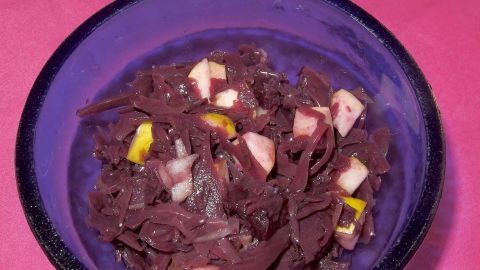 Ein bunter Rotkohlsalat in einer blauen Schüssel zeigt fein gehobelten Rotkohl, gewürzt und kombiniert mit Apfelstücken.