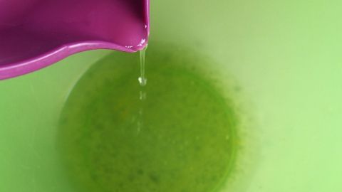 Ein lila Behälter gießt Zitronensaft in eine grüne Schüssel, um Eischnee schneller steif zu schlagen.