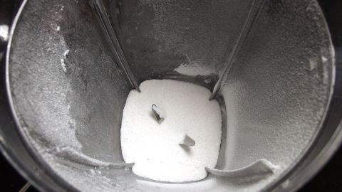 Ein Mixerbehälter enthält weißen Zucker, der zerkleinert wird, um Puderzucker selbst herzustellen.