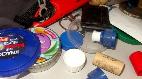 Auf einem Tisch liegen verschiedene Krimskrams-Objekte, während ein blaues Döschen geöffnet und andere Dinge daneben verstreut sind.
