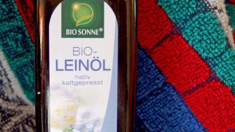 Eine Flasche Bio-Leinöl steht auf einem bunten, gestreiften Tuch, das die Verwendung von Leinöl zur Hautpflege andeutet.