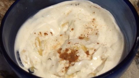 In einer blauen Schüssel liegen Bananen in Joghurt, garniert mit einer Prise Zimt, in einer modernen Küche.