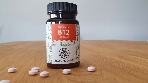 Ein Fläschchen mit Vitamin B12 steht auf einem Holztisch, umgeben von einigen Tabletten, die gegen hartnäckige Pickel helfen.