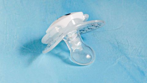 Ein Nuckel liegt auf einer blauen Fläche. Er ist transparent mit einem weißen Griff und symbolisiert die Nuckel-Entwöhnung bei Kleinkindern.