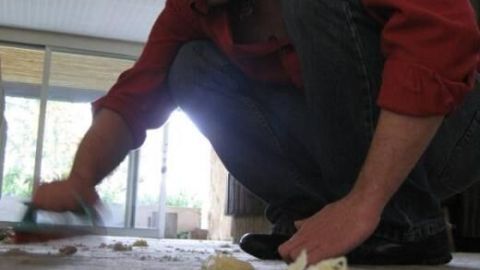 Ein Mann sitzt auf dem Boden und reinigt einen Orientteppich mit Sauerkraut, während er konzentriert arbeitet.