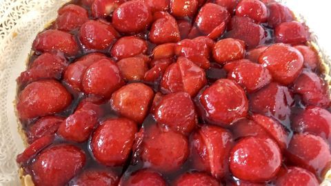 Ein runder Erdbeerkuchen wird serviert, auf dem frische Erdbeeren in einer glänzenden Wackelpudding-Schicht liegen.