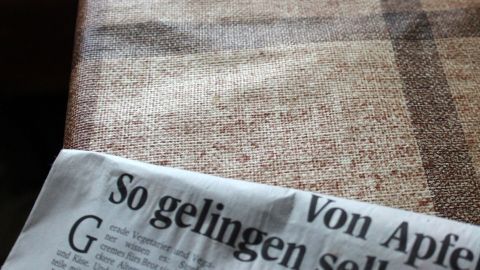 Eine Zeitung liegt auf einer Wachstuchtischdecke und zeigt einen Artikel über das Gelingen von Apfelgerichten.