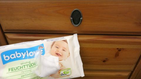 Babytücher der Marke "babylove" reinigen rustikale Holzmöbel mit einfachem Wisch; Packung zeigt lächelndes Baby.