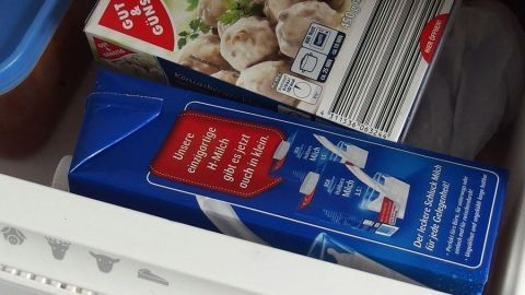 Eine blaue Milchpackung liegt im Gefrierfach, um Milch auf Vorrat zu kaufen und einzufrieren. Daneben befinden sich weitere Lebensmittel.