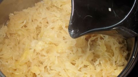 Naturreiner Apfelsaft zum geschmacklichen Aufwerten von Sauerkraut. Ein Topf mit dampfendem Sauerkraut wird aus einem schwarzen Behälter befüllt, um den Geschmack zu verbessern.