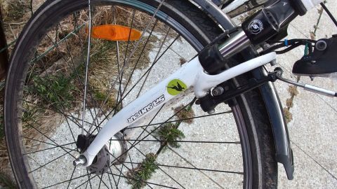 Ein Fahrrad steht auf dem Boden, während es vor Rost geschützt wird. Es ist sonnig und die Umgebung ist grün.
