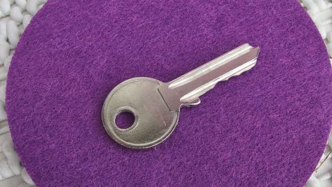 Ein Metall-Haustürschlüssel liegt auf einem lila Untergrund, bereit zum Einsatz, um nicht in der Wohnung vergessen zu werden.