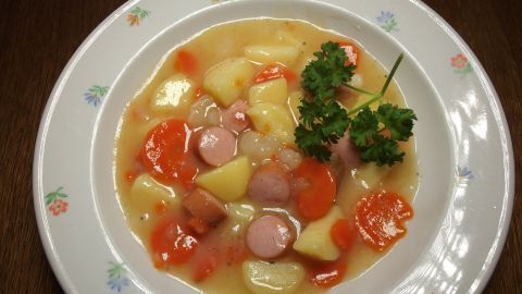 Ein Teller mit Möhreneintopf, gefüllt mit Möhren, Kartoffeln und Würstchen, garniert mit Petersilie.