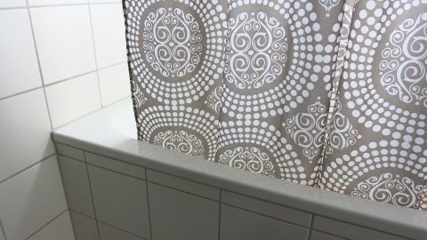 Ein Duschvorhang aus einem modernen Muster hängt in einer gefliesten Dusche, um den Raum vor Spritzern zu schützen.