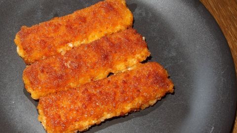 Drei goldbraune Fischstäbchen liegen auf einem schwarzen Teller, bereit zum Verzehr in einer gemütlichen Küche.