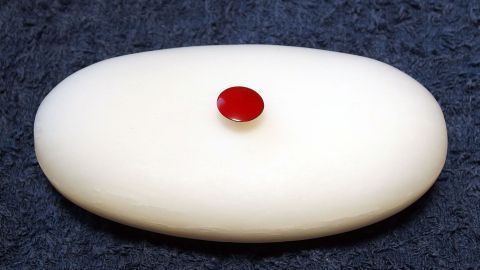 Ein ovaler, weißer Gummi mit einer roten Reißzwecke in der Mitte liegt auf einem dunklen Untergrund und zeigt eine einfache aber effektive Verwendung.