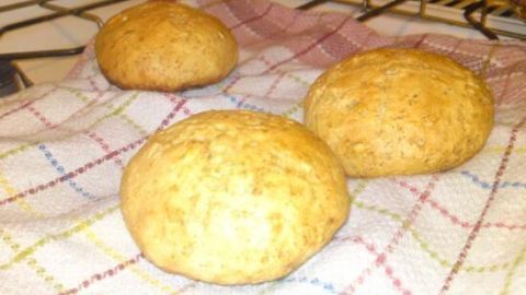 Drei goldbraune Weizenbrötchen liegen auf einem karierten Geschirrtuch, während sie abkühlen.