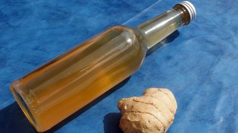 Eine Flasche mit einer würzigen Flüssigkeit steht neben frischem Ingwer auf einem blauen Untergrund, ideal gegen Reisekrankheit.