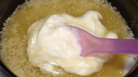 Eine beruhigende Gesichtsmaske wird mit einem pinken Spatel aus einer Mischung aus gelben und weißen Zutaten entnommen.