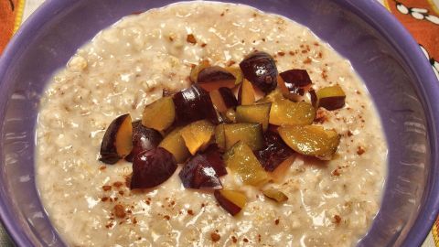 Eine Schüssel Porridge wird mit frischen, bunten Obststücken garniert und steht auf einem bunten Tisch.
