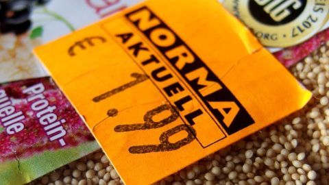 Ein orangefarbener Preisaufkleber mit "NORMA AKTUELL" und einem Preis von 1,99 € auf einem Untergrund aus verschiedenen Verpackungen.