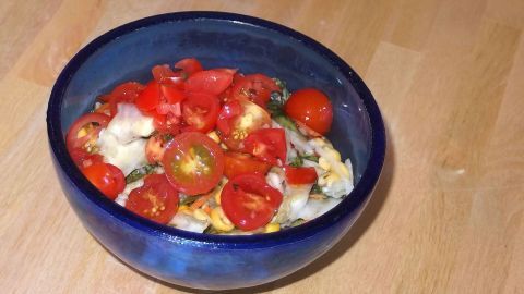Eine blaue Schüssel enthält frisch geschnittene Tomaten, die mit Pesto und anderen Zutaten zubereitet sind.