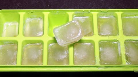 Eiswürfel aus Tee liegen in einer grünen Eiswürfelschale, einige schmelzen, ideal bei Halsschmerzen.
