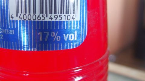 Eine rote Getränkeflasche zeigt auf dem Etikett einen Alkoholgehalt von 17% vol, platziert auf einem Tisch.