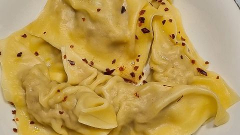 Angebraten mit etwas Butter, Öl, Zwiebeln und Paniermehl schmecken die Maultaschen vom Vortag fantastisch. Auf einem weißen Teller liegen dampfende Maultaschen, die mit roten Chiliflocken bestreut sind, auf einem Holztisch.