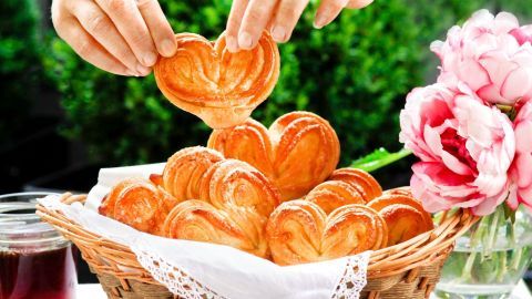 In einem Korb liegen kunstvoll geformte Schweineohren, während eine Hand ein Stück herausnimmt, um es zu genießen.