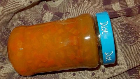 Ein Glas mit Karottenmarmelade steht auf einer karierten Decke, gefüllt mit leuchtend orangefarbener Marmelade.