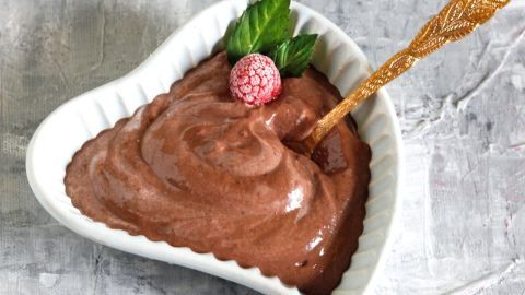 Eine herzförmige Schüssel enthält cremige Mousse au Chocolat, garniert mit einer Himbeere und Minzblättern, bereit zum Genießen.