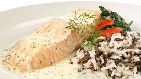 Zartes Filet mit cremiger Soße liegt neben gedämpftem Reis und frischem Gemüse auf einem weißen Teller.
