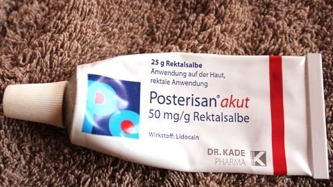 Eine Tube Hämorrhoiden-Creme liegt auf einem weichen, braunen Untergrund. Die Creme wird als topische Behandlung beworben.