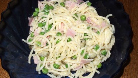 Ein Spaghettisalat mit Schinken liegt in einer blauen Schüssel und ist mit Erbsen und einer cremigen Sauce angerichtet.