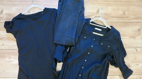 Dunkle Kleidung, bestehend aus T-Shirts, Bluse und Jeans, auf hellbraunem Holzfußboden liegend, wirkt schlankmachend.